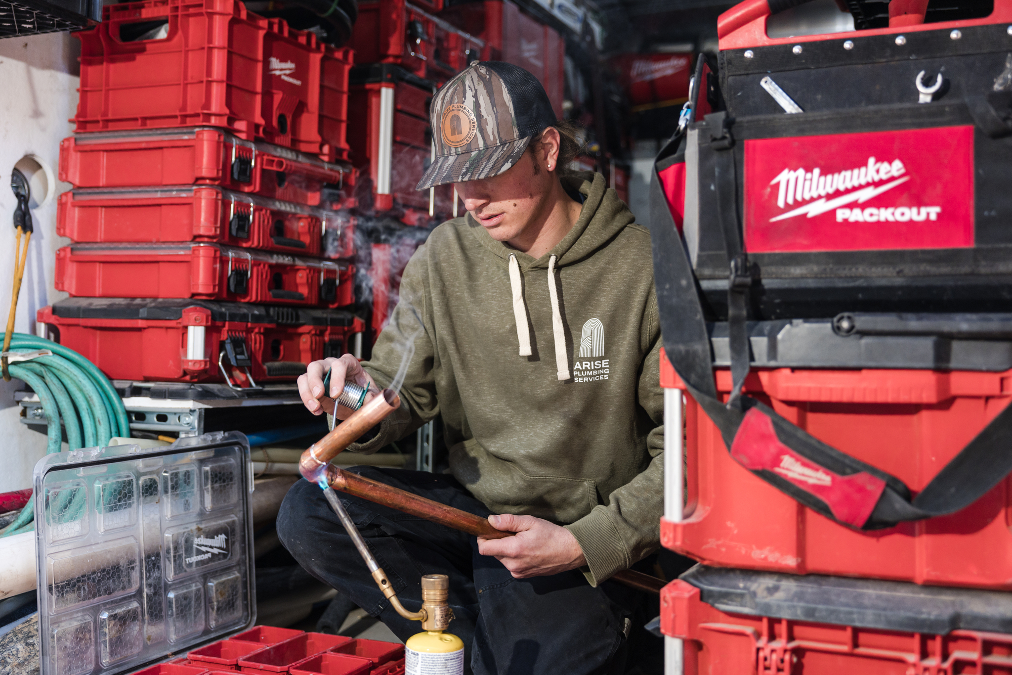 Plumber cutting copper pipe beside tool cases in an Arise work van