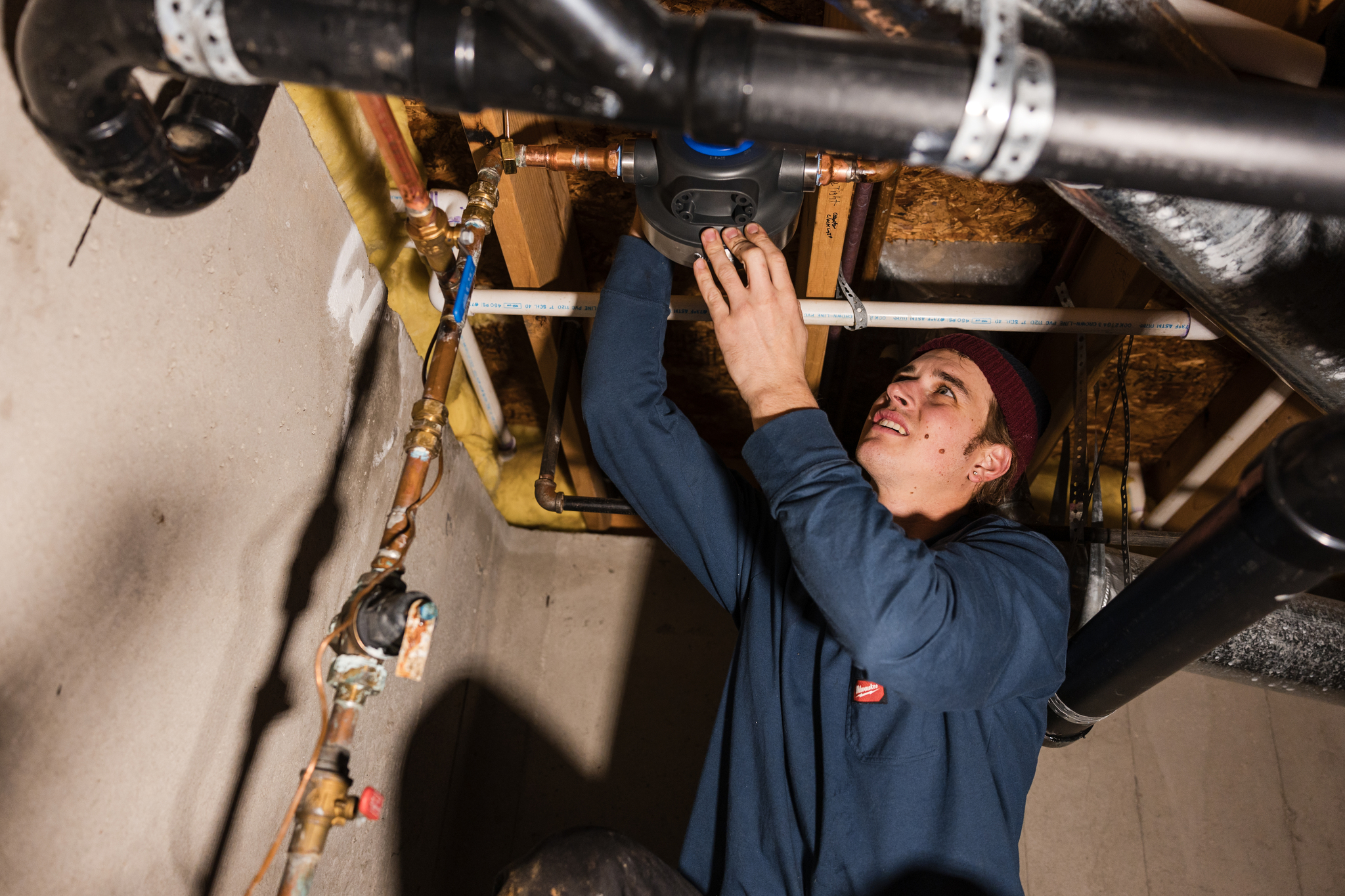 Plumber working on overhead drain and supply pipes in a basement