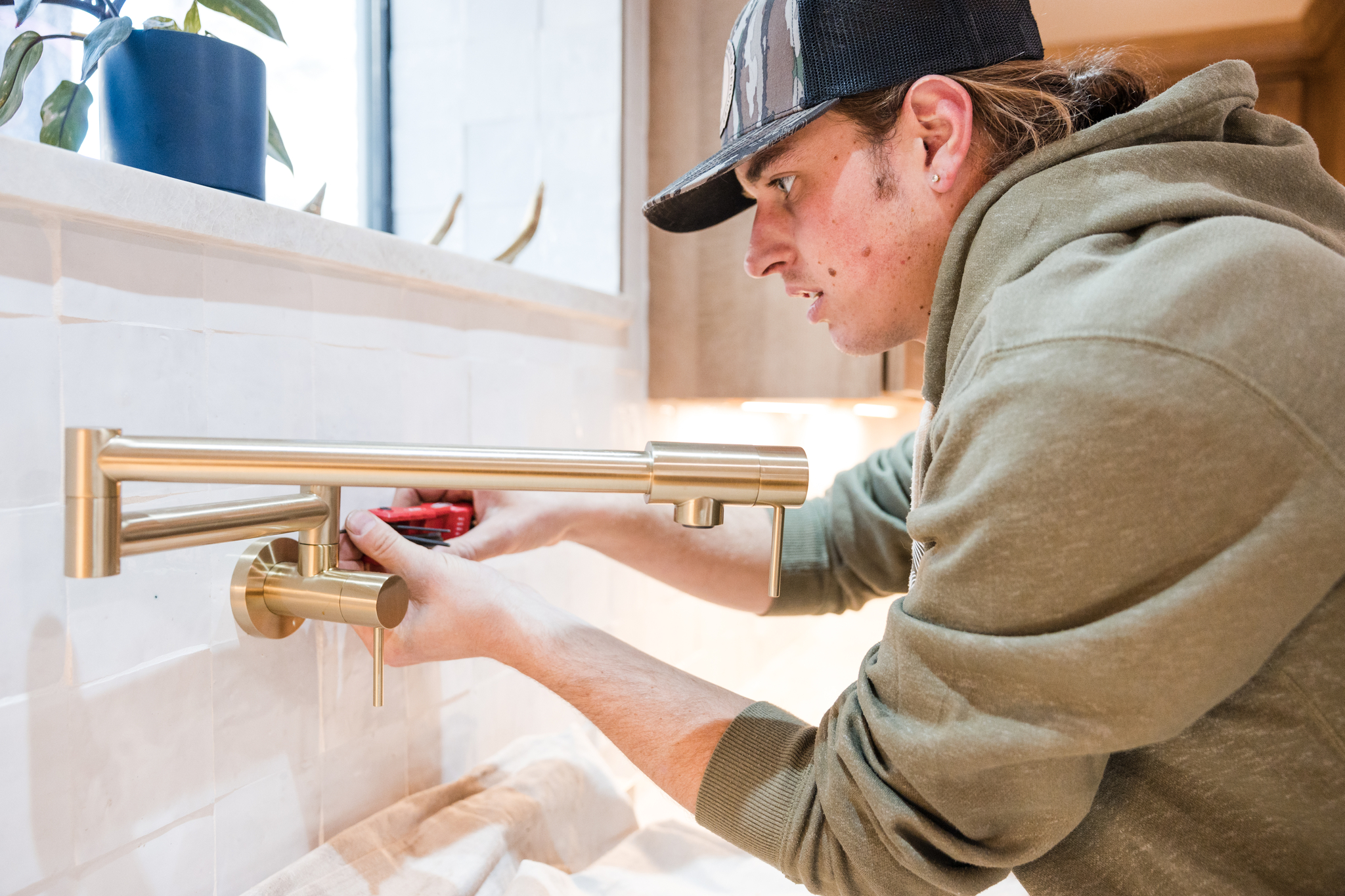 Plumber installing a brass pot filler faucet above a kitchen range